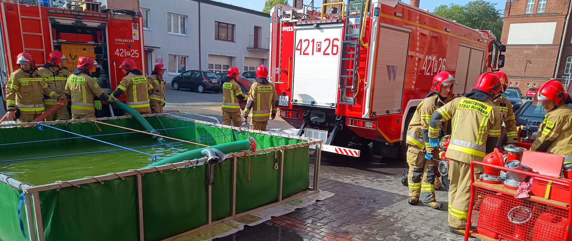 Na zdjęciu widać samochody pożarnicze oraz strażaków podczas ćwiczeń z zaopatrzenia wodnego