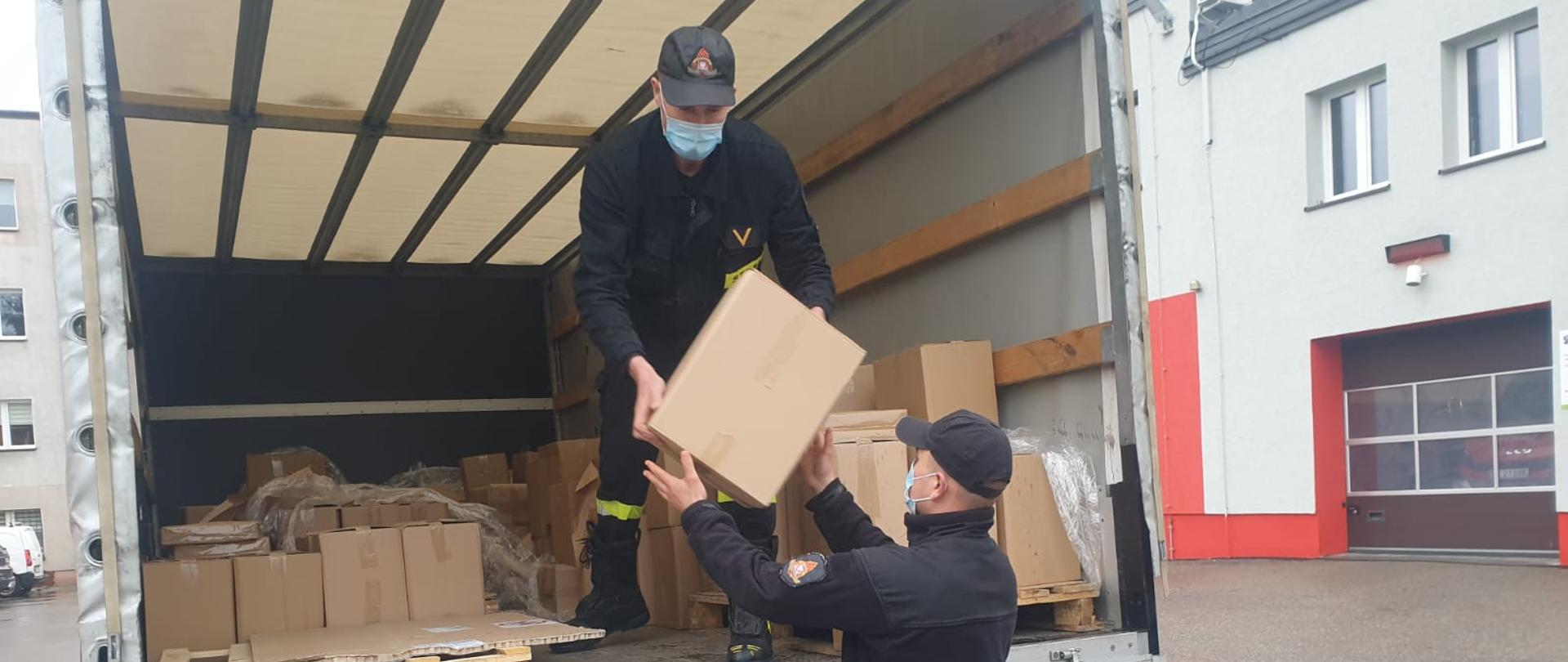 Strażacy rozładowują pudełka z ulotkami z samochodu ciężarowego