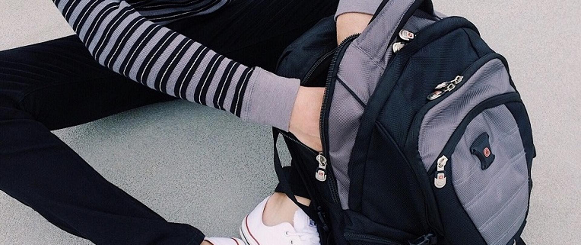 uczeń siedzący na podłodze z otwartym plecakiem