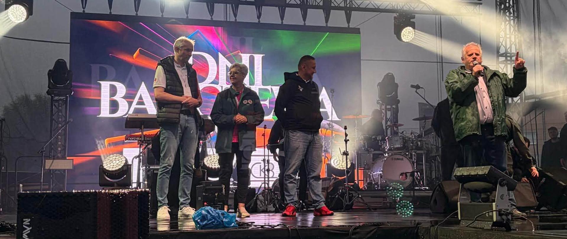 grupa oficjeli, w tym wicewojewoda, stoją na scenie, wicewojewoda przemawia, jest wieczór