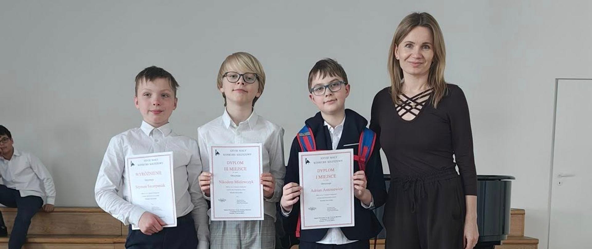 Klaudia Jarczyńska pozuje na stojąco wraz z trójką swoich uczniów trzymających dyplomy