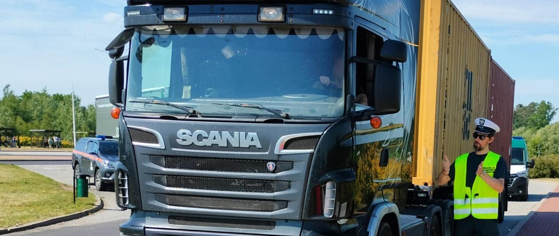 Wieloosiowy samochód ciężarowy przed wjazdem na wagi, obok kierujący nim Inspektor transportu drogowego.