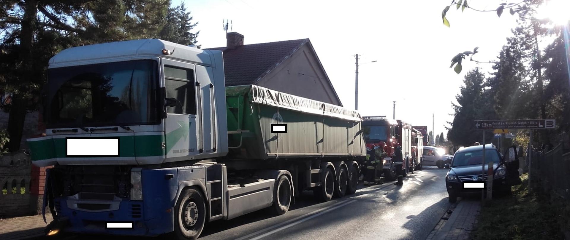 Strażacy prowadza działania ratownicze, w tle uszkodzone pojazdy