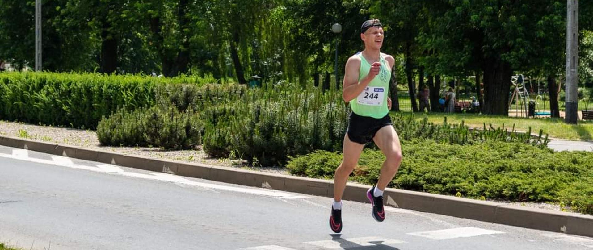 młody mężczyzna w stroju sportowym podczas biegu ulicznego, w tle fragmenty parku miejskiego