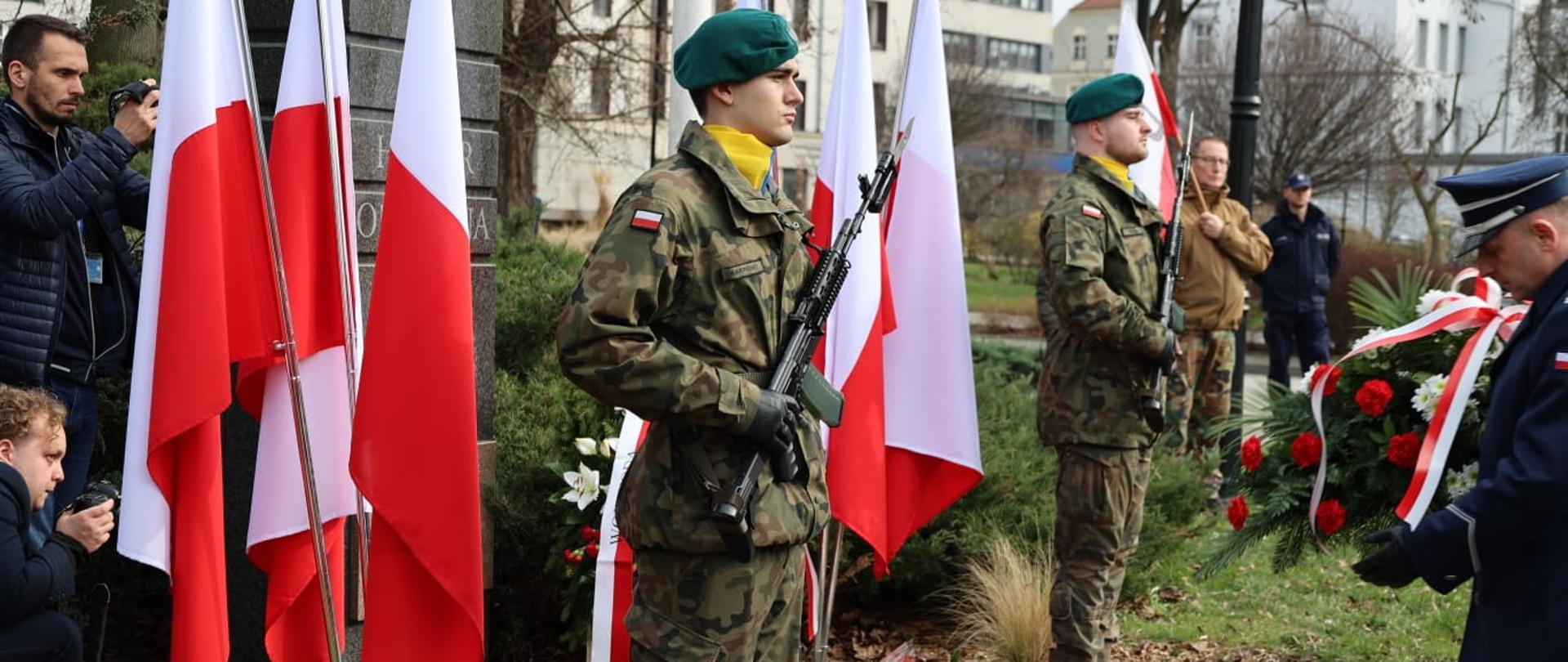 Obchody Narodowego Dnia Pamięci Żołnierzy Wyklętych przy Placu Wolności w Opolu. Na zdjęciu widać złożone kwiaty, dwóch żołnierzy stojących obok, polskie flagi i znicze. 