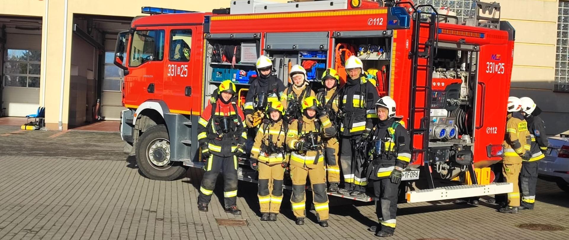 Słuchacze kursu pozują do zdjęcia na tle samochodu pożarniczego