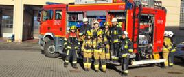 Słuchacze kursu pozują do zdjęcia na tle samochodu pożarniczego