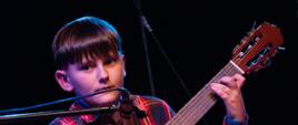 Zdjęcie przedstawia ucznia Wojciecha Czajkę występującego na gitarze podczas koncertu świątecznego.