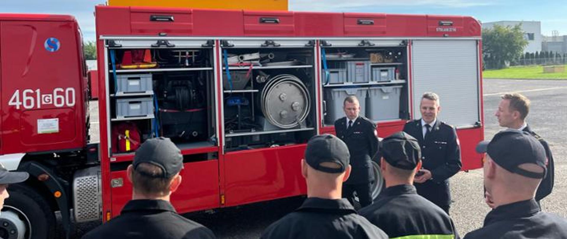 grupa strażaków stoi przy samochodzie strażackim