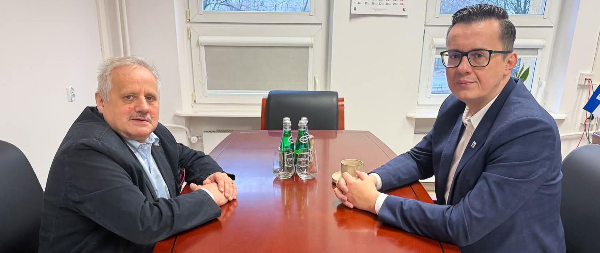 Dwóch mężczyzn siedzi przy stole i rozmawia. 