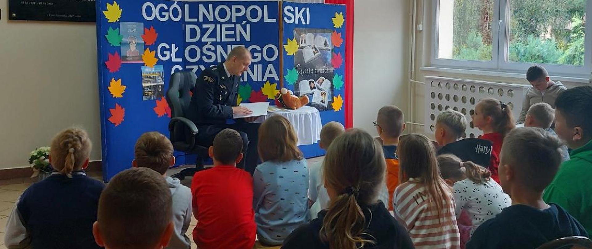 Zastępca komendanta powiatowego PSP w Ostródzie czyta dzieciom książkę. 