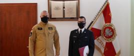 dwóch mężczyzn stoi w maseczkach ochronnych na twarzach. jeden z nich ubrany w miosdowy mundur. drugi w okularach w ciemnym mundurze z białą koszulą , w ręku trzyma teczkę