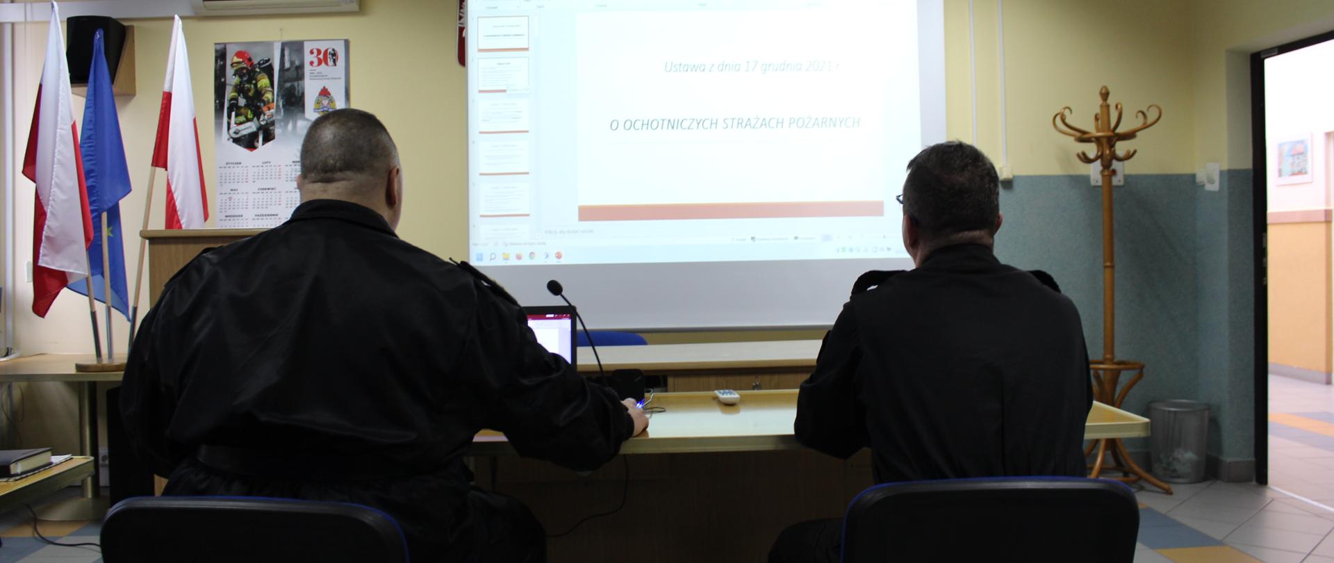Komendant Miejski PSP w Łomży prezentuje założenia Ustawy o Ochotniczych Strażach Pożarnych na wideokonferencji. w tle na rzutniku przedstawiane są założenia w/w ustawy