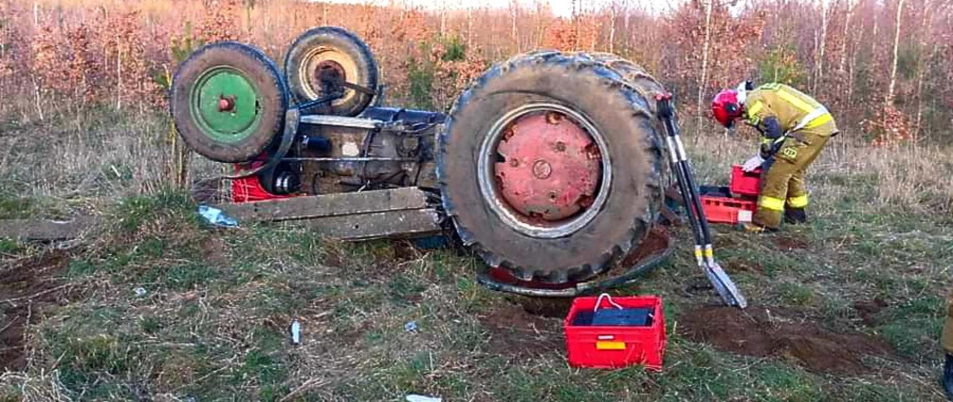 Traktor do góry kołami oraz strażak podczas działań ratowniczych