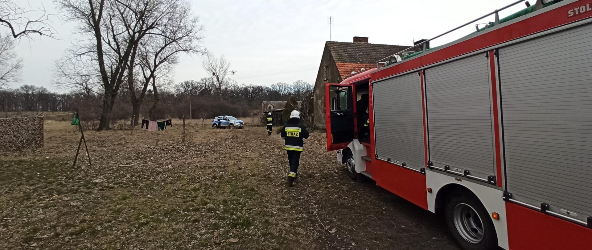 Zdjęcie przedstawia akcję ratowniczą w Torzeńcu, gdzie doszło do zaczadzenia dwóch osób ze skutkiem śmiertelnym. Na zdjęciu widzimy pojazd ratowniczo - gaśniczy oraz funkcjorariusza OSP. Zdjęcie wykonane w porze dziennej przed posesją.