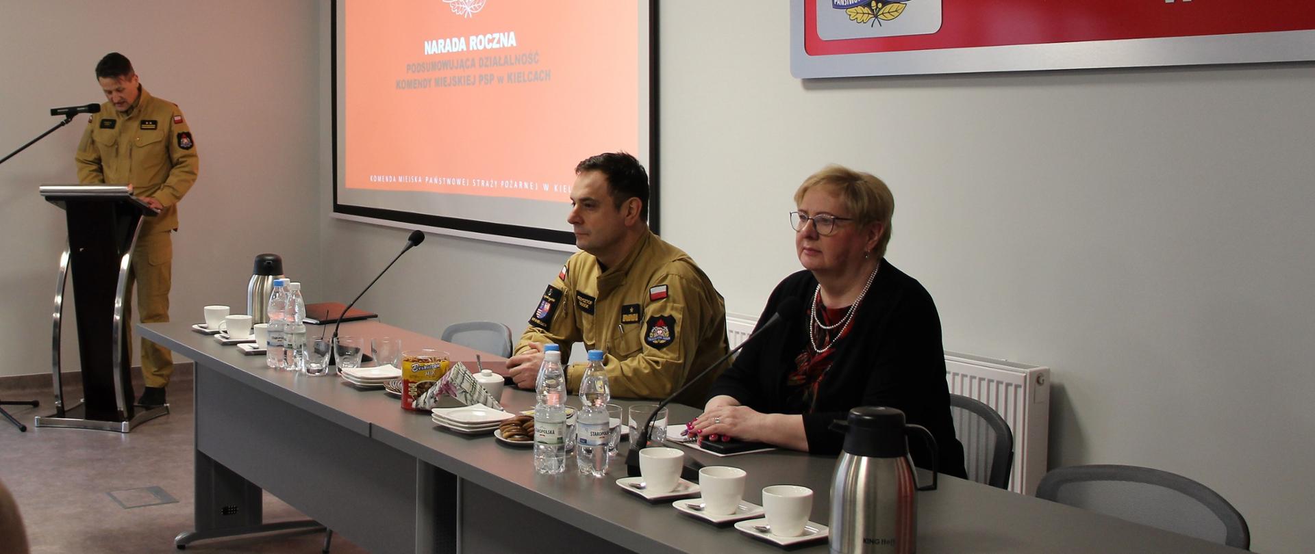 Zdjęcie przedstawia gości narady rocznej: przy stole siedzą od lewej nadbryg. Krzysztof Ciosek i pani Bożena Szczypiór. Przy mównicy głos zabiera bryg. Mariusz Góra