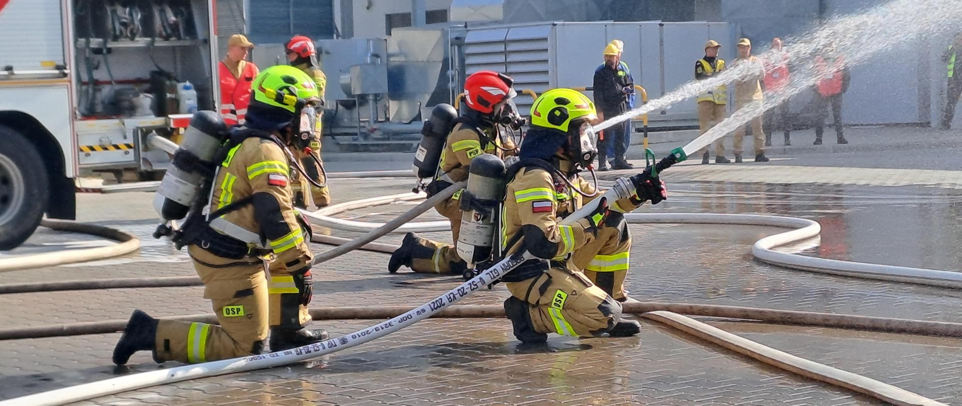 Strażacy trzymają węże z których leci woda