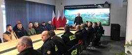 Siedzący przy stole strażacy OSP słuchają wykładu. W głębi na tle panoramy Sandomierza strażak PSP, stoi i przemawia do słuchaczy. Kliknięcie spowoduje powiększenie