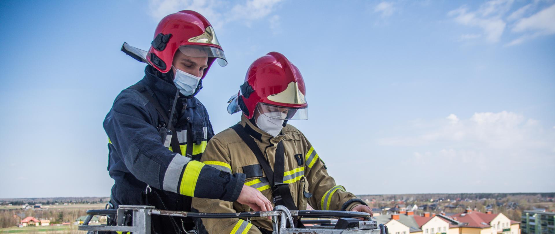 Zdjęcie przedstawia strażaków operujących drabiną mechaniczną z kosza podczas ćwiczeń.