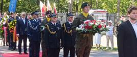 Przedstawiciele służb mundurowych oraz delegacje z wieńcami podczas uroczystości rocznicowych na terenie leśnym.