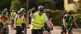 Po drodze jedzie grupa rowerzystów w żółtych odblaskowych kamizelkach, z przodu minister Czarnek podnosi rękę.