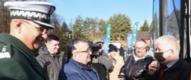 Minister Infrastruktury Andrzej Adamczyk i Główny Inspektor Alvin Gajadhur wręczają maskotę - Krokodylka Tirka kierowcy autokaru. W tle stoją dziennikarze.