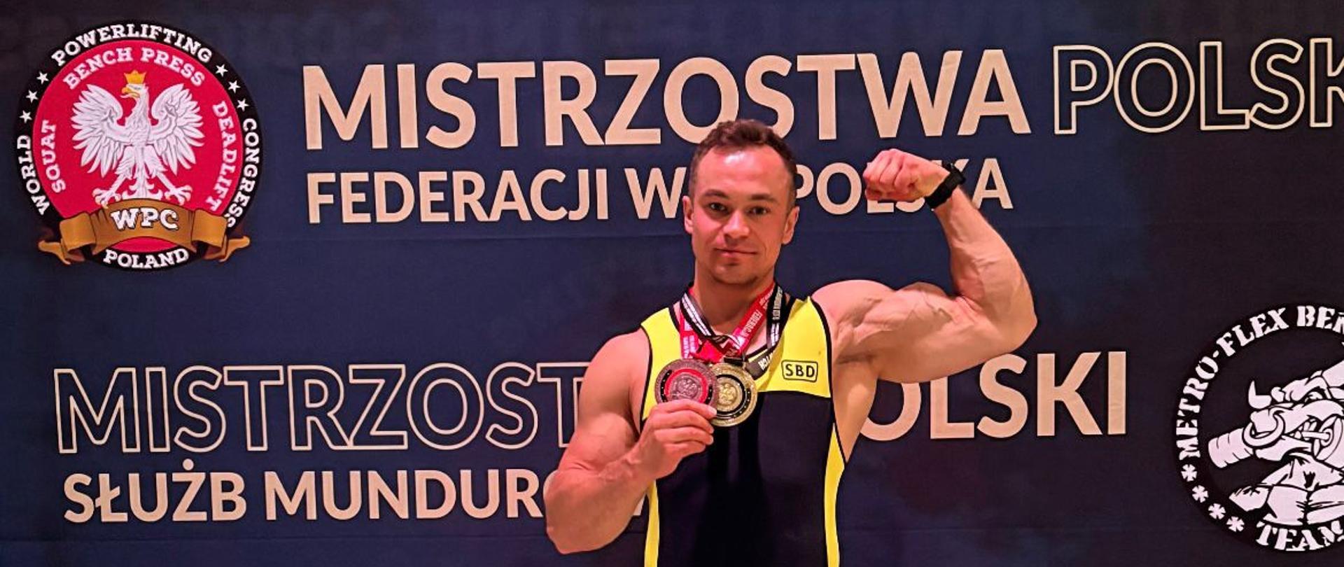 Strażak w stroju sportowym stojący na tle baneru zawodów