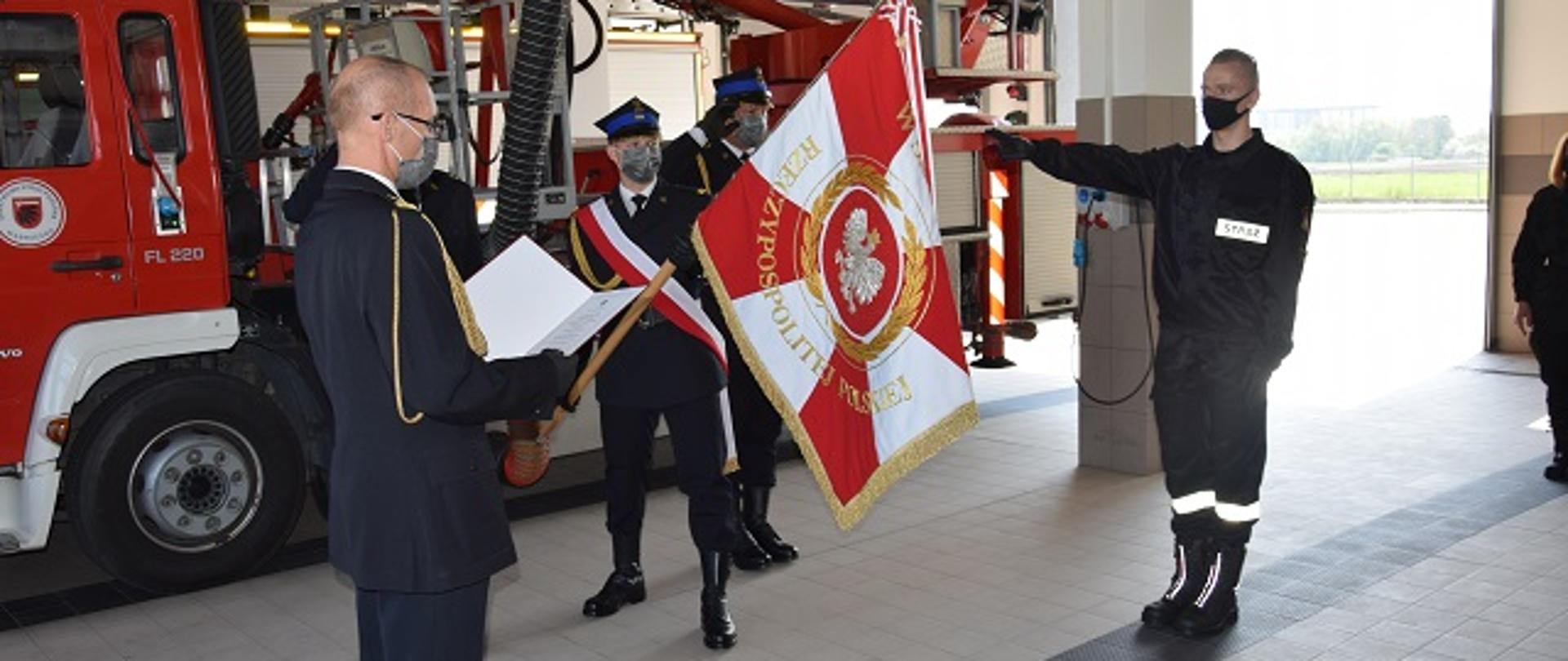 Ślubowanie strażaka Pawła Leśniewskiego złożone przed komendantem powiatowym PSP w Wąbrzeźnie st.bryg. Januszem Woźniakiem. W tle poczet sztandarowy oraz samochód SHD23.