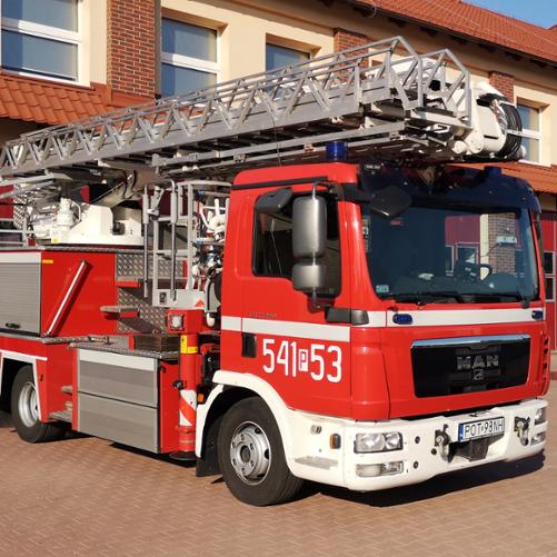 Na zdjęciu samochód specjalny typu podnośnik hydrauliczny na placu manewrowym przed garażami Jednostki Ratowniczo-Gaśniczej