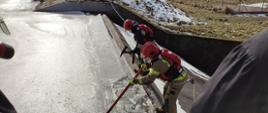Na zdjęciu widać dwóch ratowników, którzy zabezpieczeni w kamizelki ratownicze, hełmy oraz linki skuwają za pomocą bosaka oraz topora strażackiego lód na zaporze zalewu w Suchedniowie. 