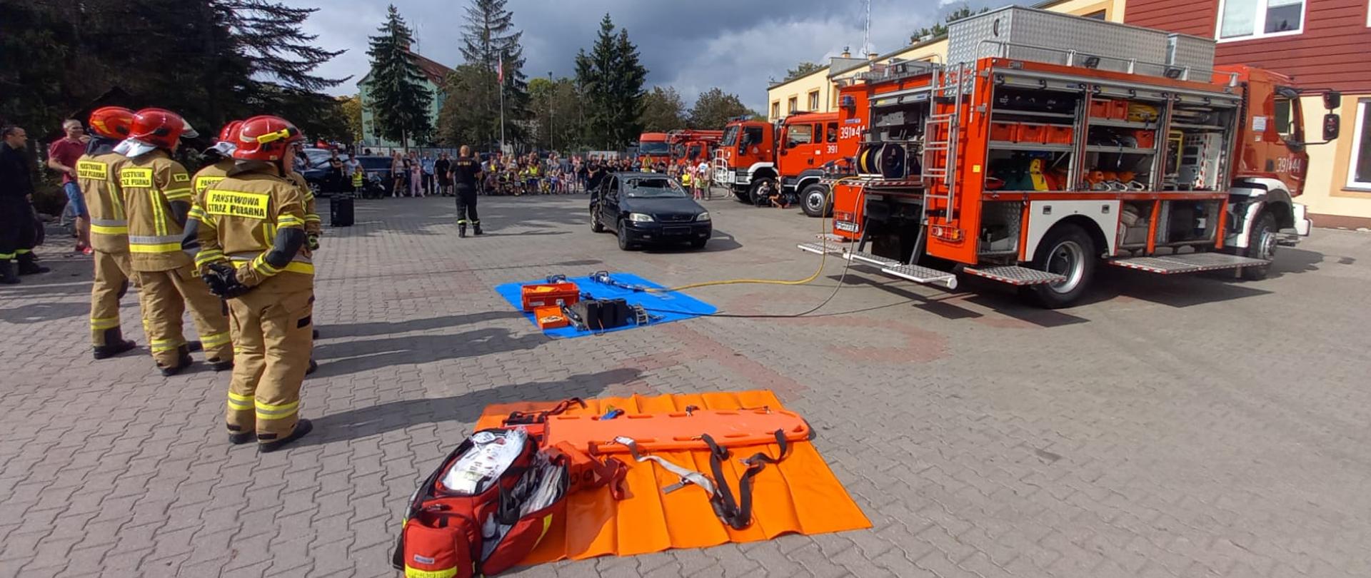 Plac wewnętrzny KP PSP w Słubicach. Po prawej stronie na tle budynku stojący samochody pożarnicze. Na wprost widoczni ustawieni ludzie. Na środku strażak z mikrofonem. Po lewej strażacy w umundurowaniu specjalnym.