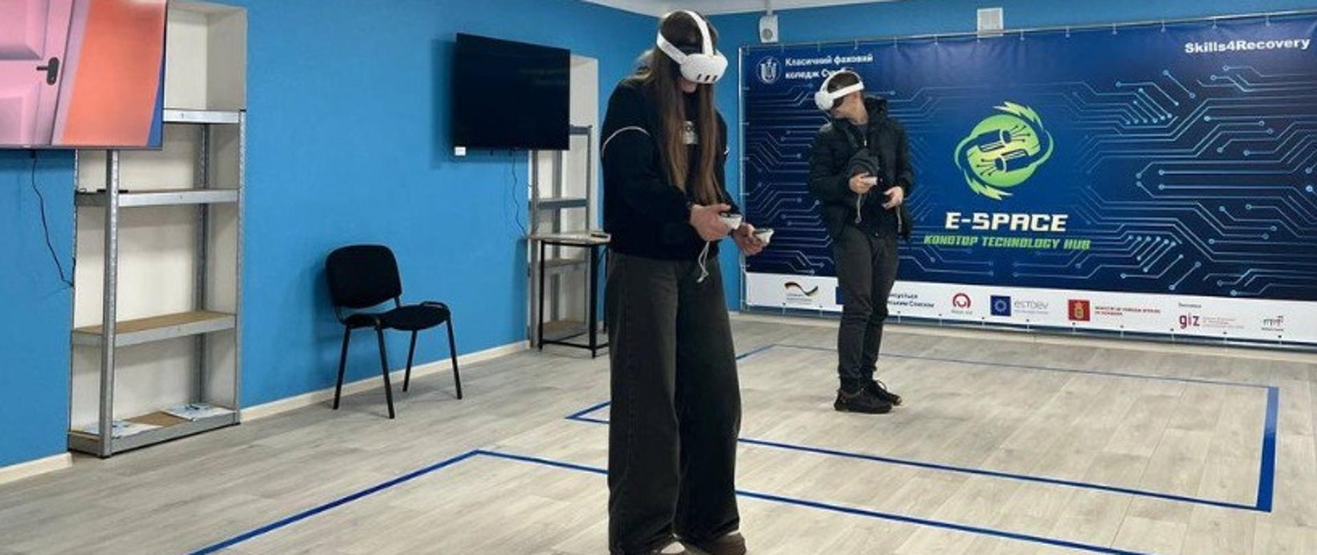 Dwie osoby stoją pośrodku sali w goglach VR i z joystickami. 