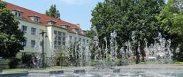 Zdjęcie przedstawia budynek szkoły w otoczeniu fontanny