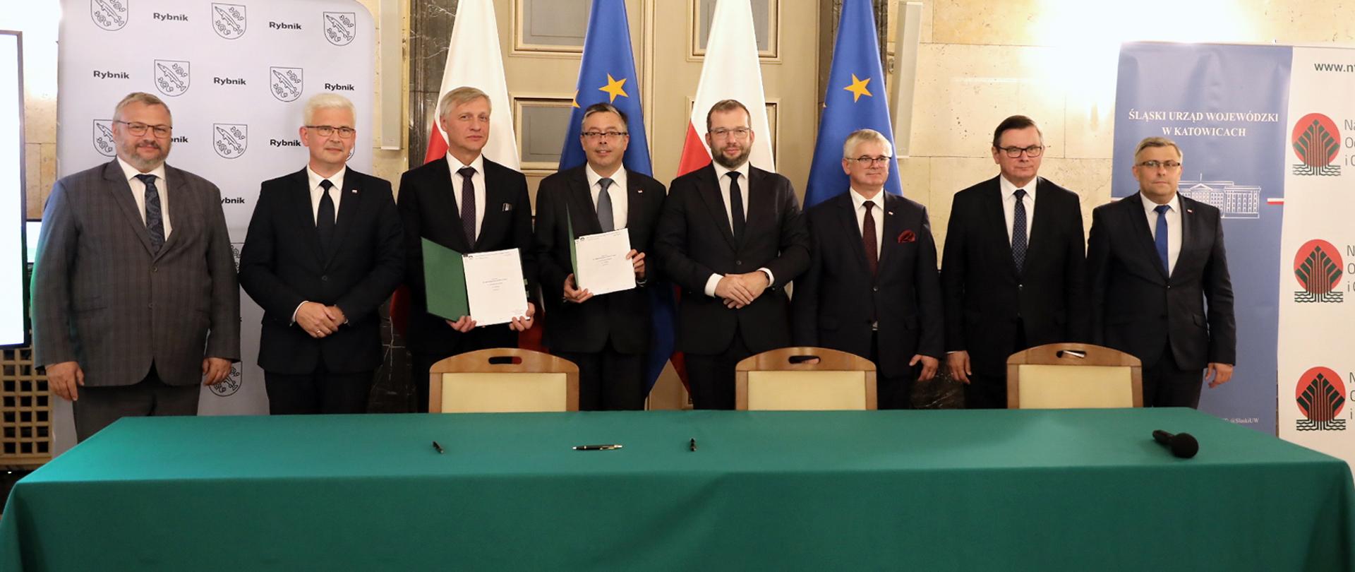 Sześciu samorządowców oraz minister Grzegorz Puda i wiceminister Ireneusza Zyska stoi w jednym rzędzie przy stole z zielonym suknem. W tle za plecami osób flagi Polski i Unii Europejskiej.