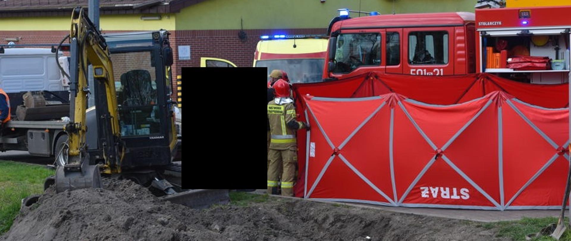 Po lewej widać koparkę, w środku rozstawiony parawan, za n im samochód strazacki