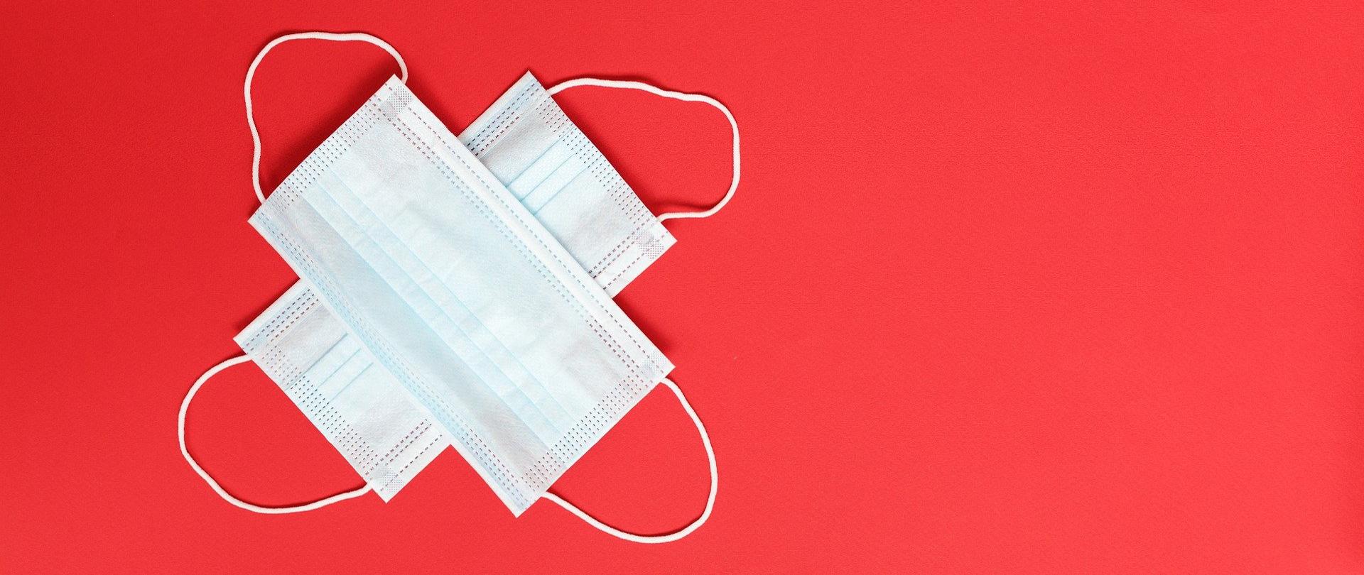 Czerwone tło, w lewym rogu dwie skrzyżowane maseczki