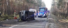 Strażacy i ratownicy medyczni podczas uwalniania osób poszkodowanych. samochód osobowy leży na boku na środku drogi. 