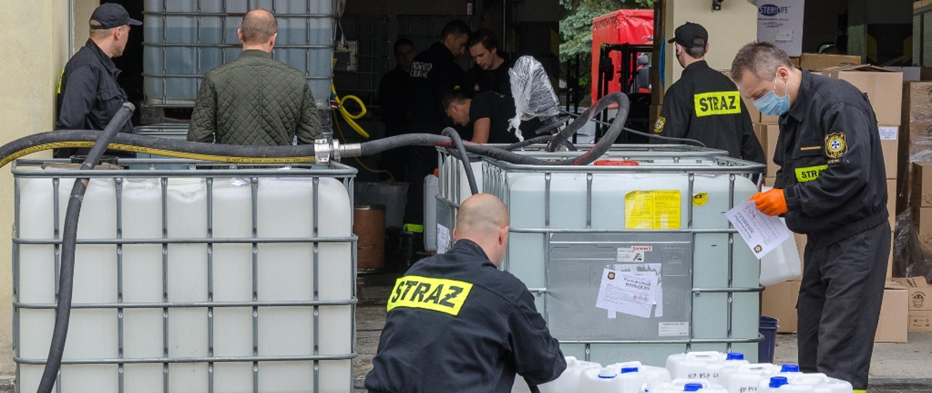 Działania mazowieckich strażaków w związku z epidemią koronawirusa – na zdjęciu strażacy rozlewają środki odkażające do mniejszych pojemników. Kilku z nich jest w maseczkach.