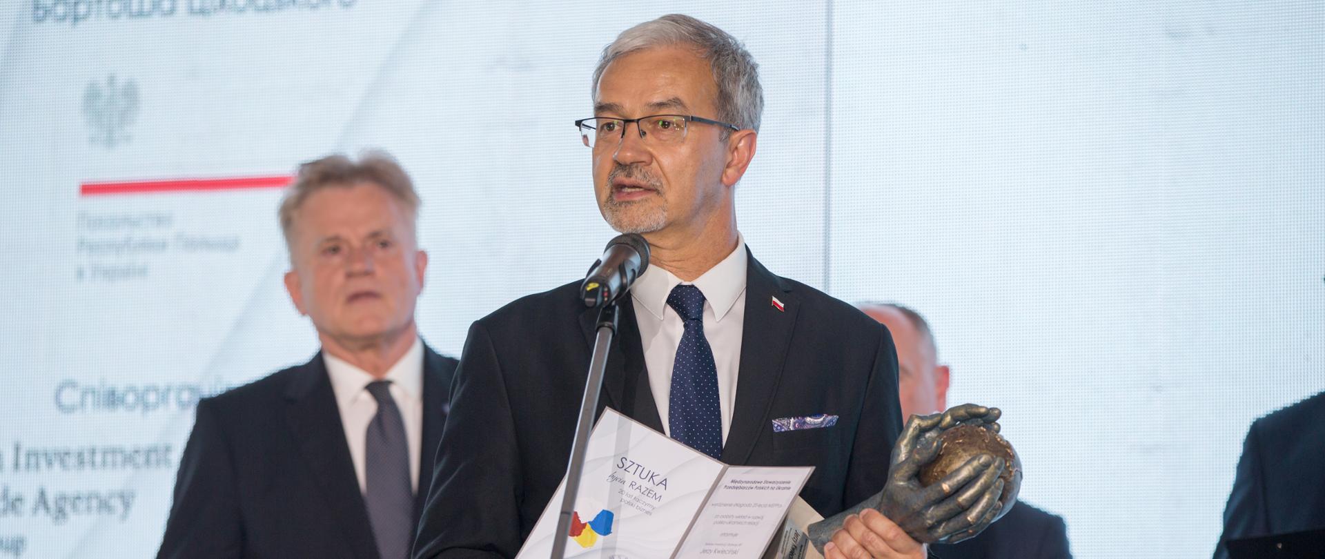 Na zdjęciu przy mikrofonie stoi minister Kwieciński, w dłoni trzyma dyplom i statuetkę 