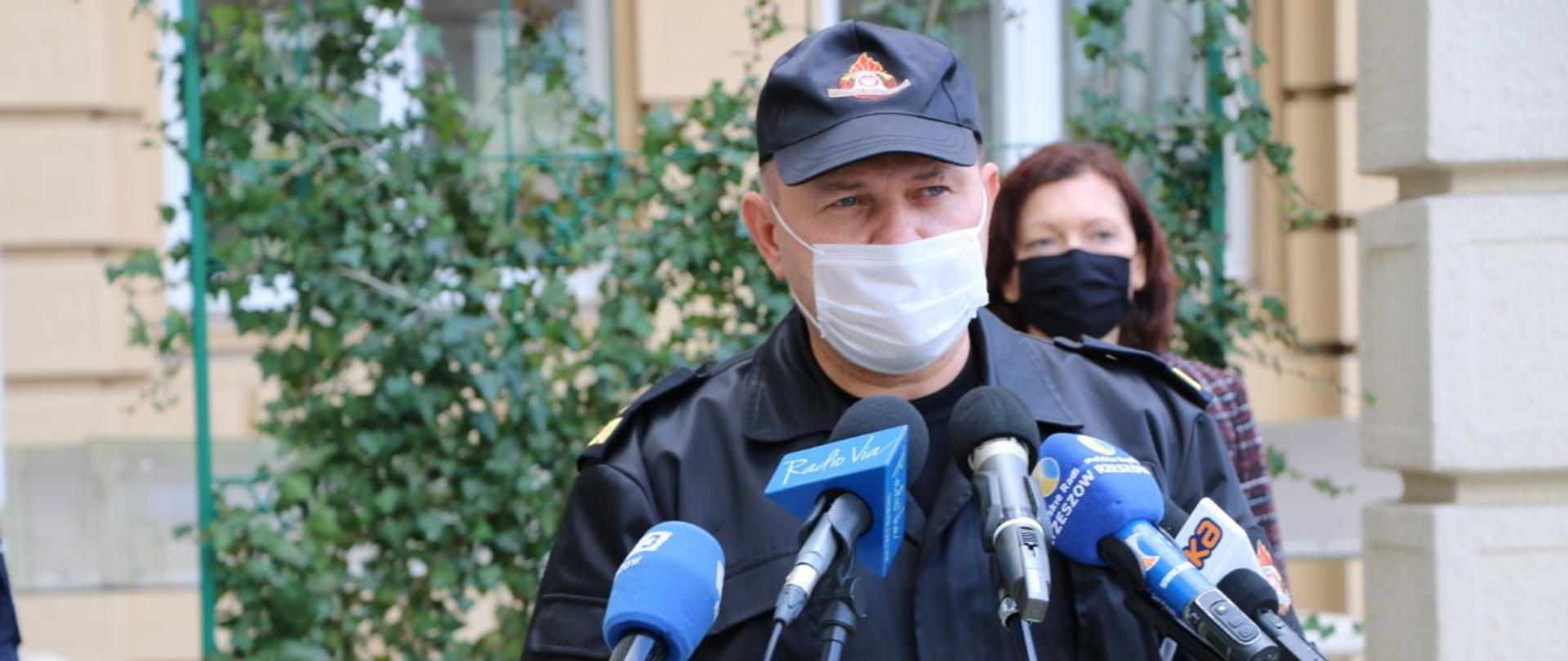 Na pierwszym planie zdjęcia nadbrygadier Andrzej Babiec stoi przed mikrofonami dziennikarzy.