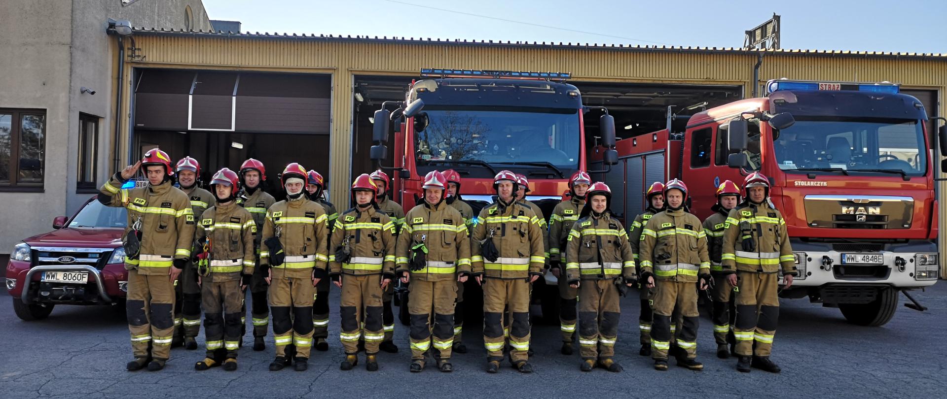 Na zdjęciu strażacy z JRG Wołomin w umundurowaniu bojowym na tle garażu w Komendzie Powiatowej oraz samochodów strażackich ustawieni w szyku podczas minuty ciszy za poległych w Ukrainie strażaków