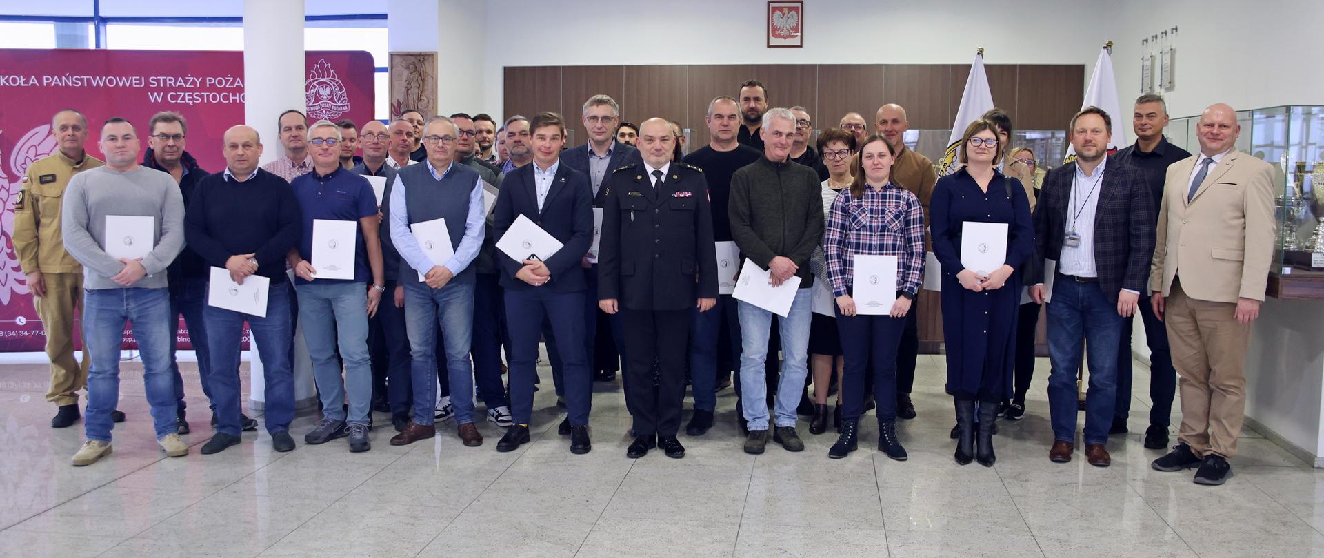 Pamiątkowe zdjęcie grupowe uczestników szkolenia z zakresu ochrony ludności i obrony cywilnej (32 osoby) w towarzystwie Komendanta Centralnej Szkoły PSP, wykładowcy na szkoleniu oraz funkcjonariusza CS PSP