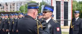 Zastępca Świętokrzyskiego Komendanta przypina wyróżnionemu strażakowi medal, za nimi kompania strażaków.