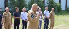 Na pierwszym planie Zastępca Komendanta Powiatowego PSP w Starachowicach st. bryg. Paweł Borek przemawia podczas zakończenia i podsumowania ćwiczeń