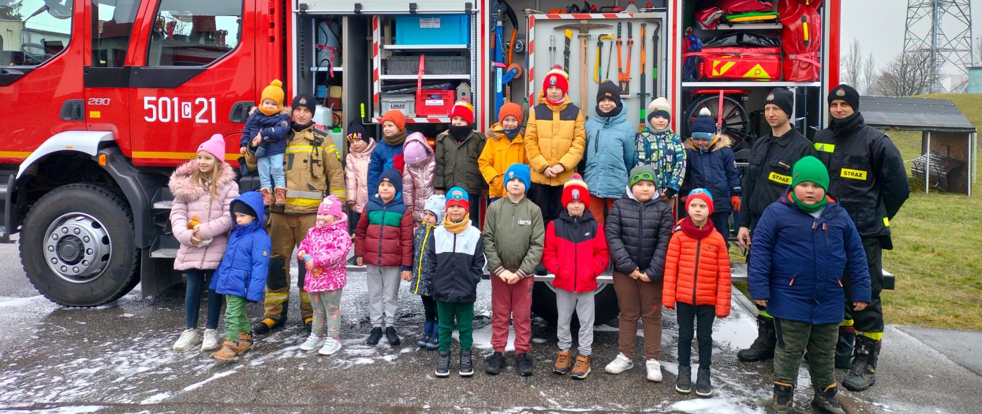 Zdjęcie przedstawia dzieci oraz strażaków podczas pokazu w związku z akcją "Bezpieczne Ferie". Na drugim planie wóz strażacki.