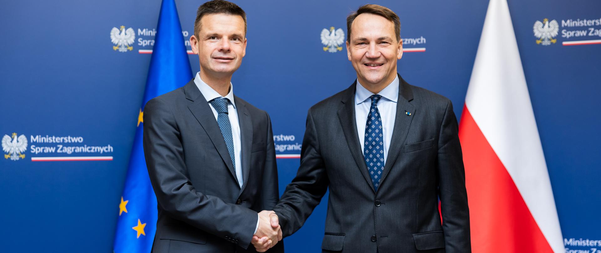Minister Radosław Sikorski z Prezesem Europejskiego Trybunału Praw Człowieka Marko Bošnjakiem podczas uścisku dłoni. W tle flagi i ścianka.