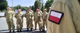 Grupa strażaków stoi na placu podczas odprawy przed wyjazdem do Austrii