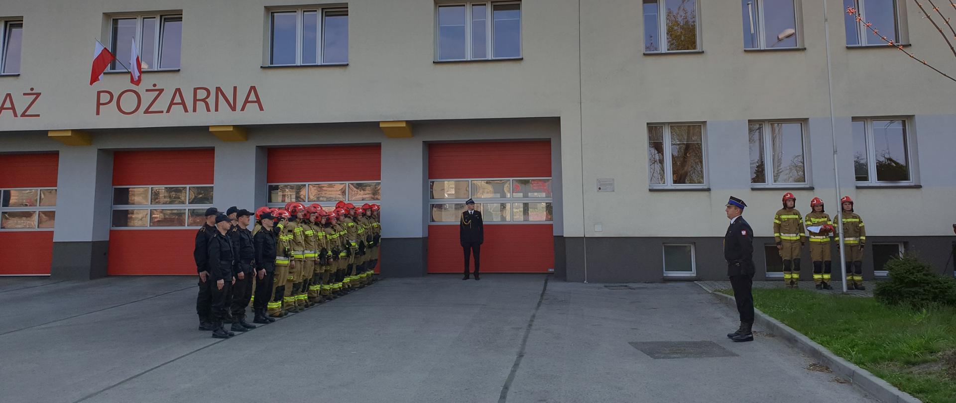 Uczczenie Dnia Flagi Rzeczpospolitej Polskiej przez jaworznickich strażaków. Na tle Komendy Miejskiej jaworzniccy strażacy wywieszają flagę na maszt.