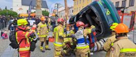 Na zdjęciu strażacy podczas zawodów z ratownictwa technicznego uwalniają osobę poszkodowaną z samochodu osobowego. W tle ludzie obserwujący zmagania strażaków.