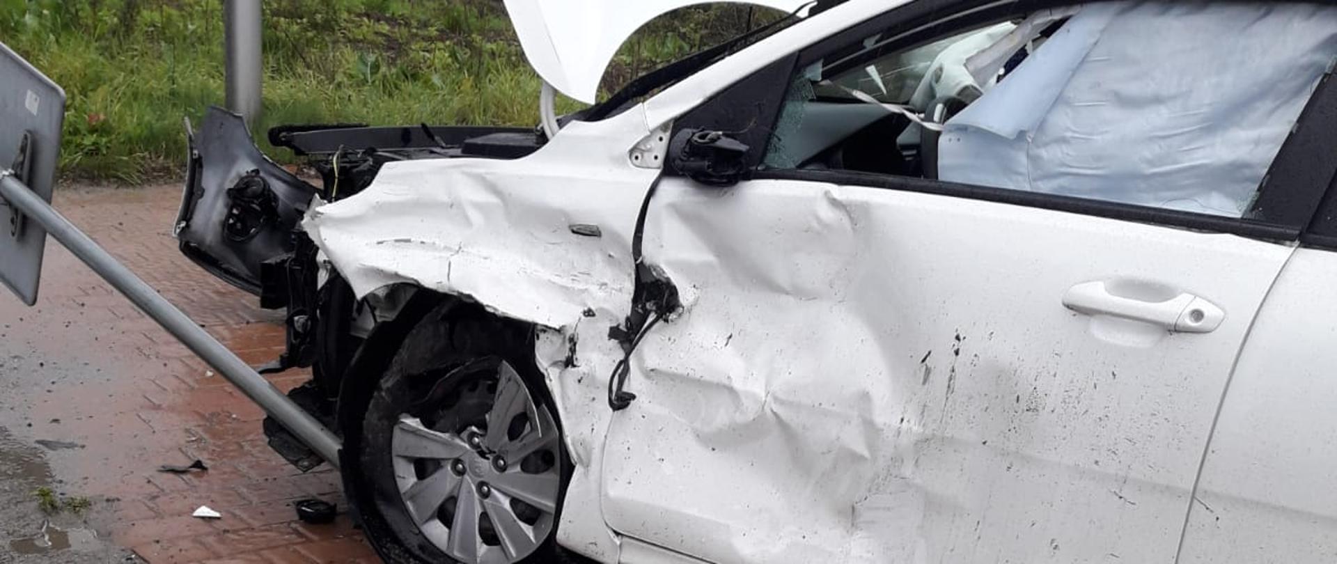 Biały samochód uszkodzony. Przednie kola na jechały na znak drogowy.